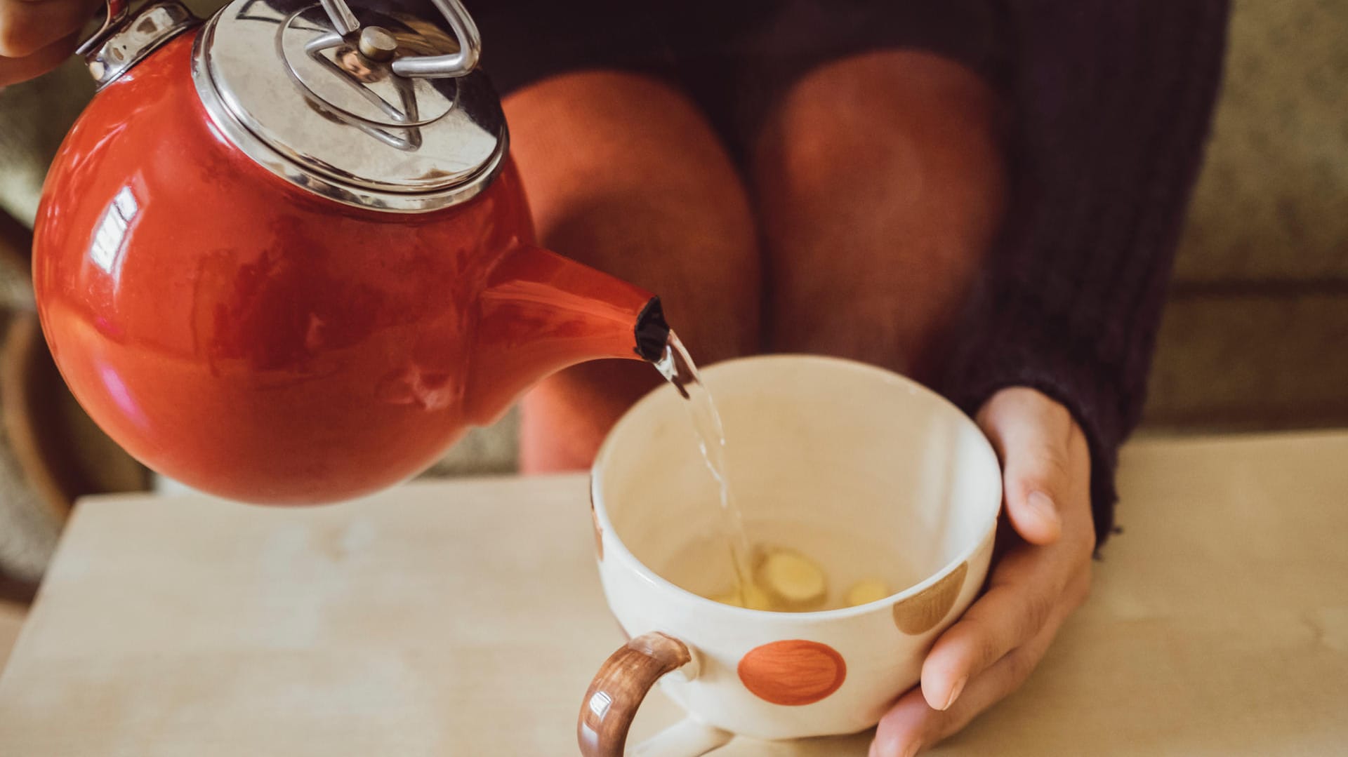 Eine Frau gießt heißes Wasser in eine Tasse mit frischem Ingwer. Die scharfe Knolle gibt dem Immunsystem den richtigen Kick.