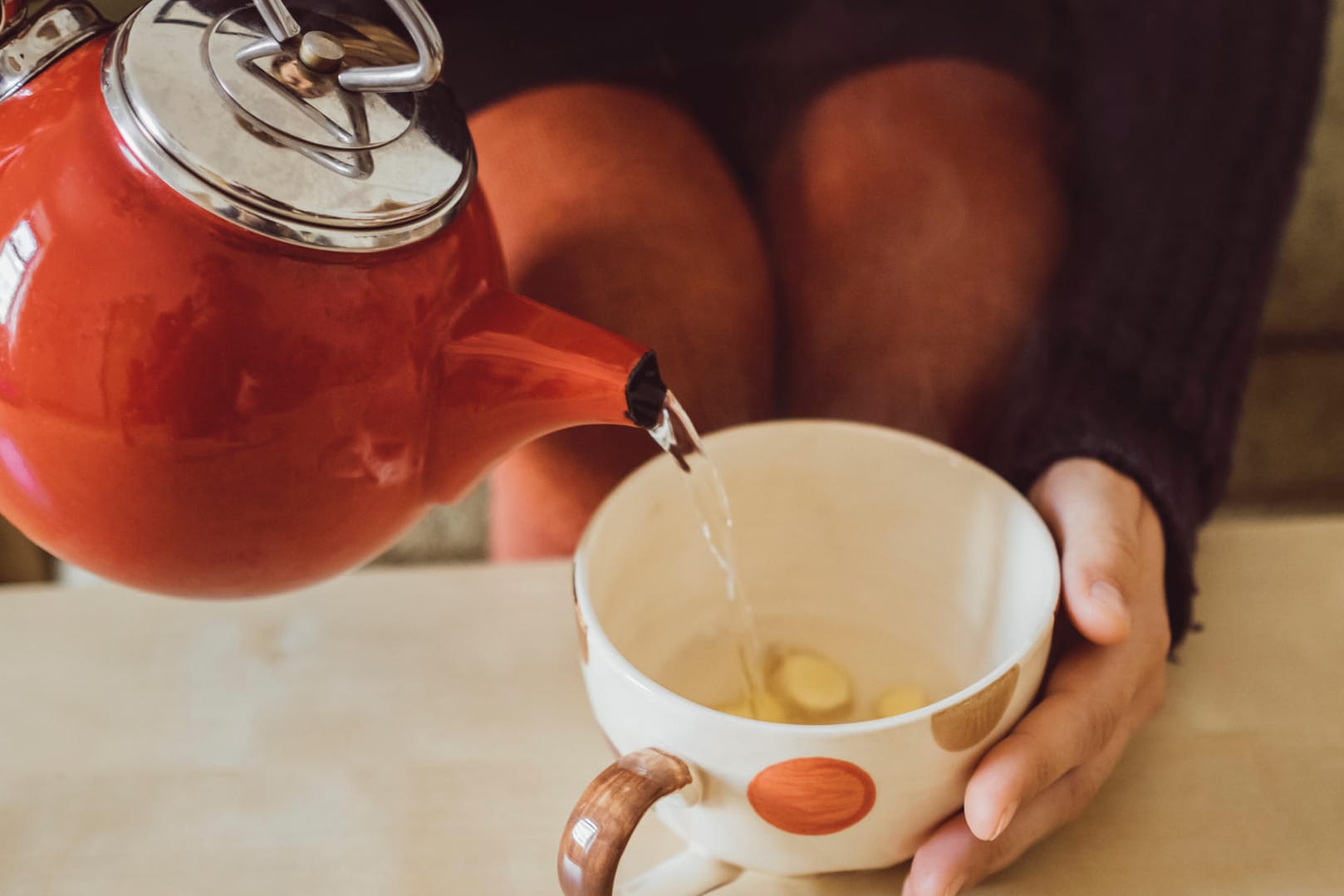 Eine Frau gießt heißes Wasser in eine Tasse mit frischem Ingwer. Die scharfe Knolle gibt dem Immunsystem den richtigen Kick.