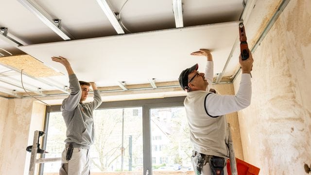 Handwerkliches Geschick ist ein Muss für angehende Stuckateure: Azubi Jonas Schwarzwälder (l) und sein Ausbilder Egon Karl (r) schrauben eine Rigips-Platte an die Decke einer Wohnung.