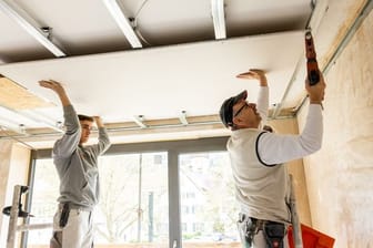 Handwerkliches Geschick ist ein Muss für angehende Stuckateure: Azubi Jonas Schwarzwälder (l) und sein Ausbilder Egon Karl (r) schrauben eine Rigips-Platte an die Decke einer Wohnung.