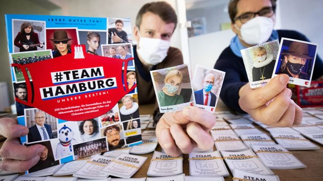 Alexander Böker (l) und Oliver Wurm halten Panini-Sammelalbum "#Team Hamburg" in der Hand: Der Erlös wird noch im Mai von einem Gremium an die Kulturszene in Hamburg verteilt.