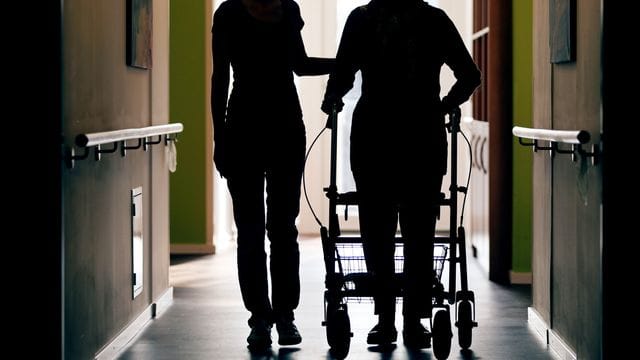 Eine Pflegerin (l) begleitet die Bewohnerin eines Altenheims beim Gang über den Flur. Eine Pflegerin (l) begleitet die Bewohnerin eines Altenheims beim Gang über den Flur.