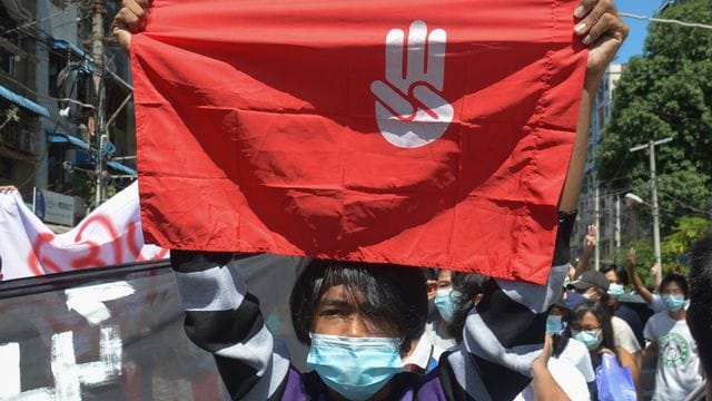 Ein Protestteilnehmer hält während einer Demonstration in Yangon eine Flagge hoch, auf der das Drei-Finger-Zeichen des Widerstandes zu sehen ist. Ein Protestteilnehmer hält während einer Demonstration in Yangon eine Flagge hoch, auf der das Drei-Finger-Zeichen des Widerstandes zu sehen ist.