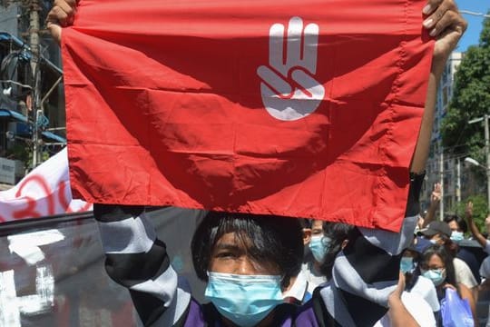 Ein Protestteilnehmer hält während einer Demonstration in Yangon eine Flagge hoch, auf der das Drei-Finger-Zeichen des Widerstandes zu sehen ist.