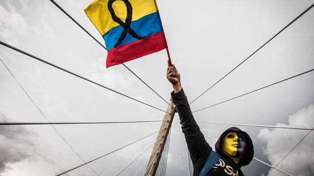 Ein maskierter Demonstrant schwenkt die kolumbianische Flagge. Ein maskierter Demonstrant schwenkt die kolumbianische Flagge.