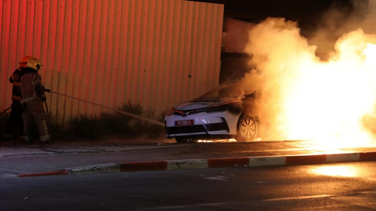 Israel, Lod: Israelische Feuerwehrleute löschen ein brennendes Polizeiauto.