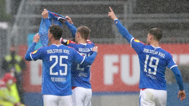 Die Kieler Spieler Phil Neumann (l-r), Hauke Wahl und Simon Lorenz halten nach dem Treffer zum 1:1 ein Trikot des verletzten Mannschaftskameraden Ahmet Arslan hoch.