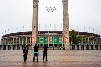 Drei Fußball-Fans stehen vor dem Olympiastadion und machen Fotos.