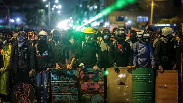 Demonstranten stehen bei einem Protest an einer Kreuzung mit Schildern und Laserpointern. Demonstranten stehen bei einem Protest an einer Kreuzung mit Schildern und Laserpointern.