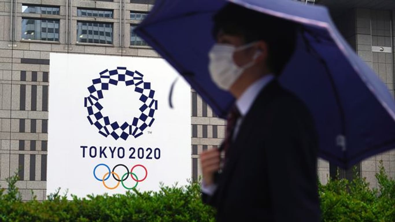 Ein Mann mit Mund-Nasen-Schutz geht im Regen an einem Banner der Olympischen Spiele Tokio 2020 vorbei.