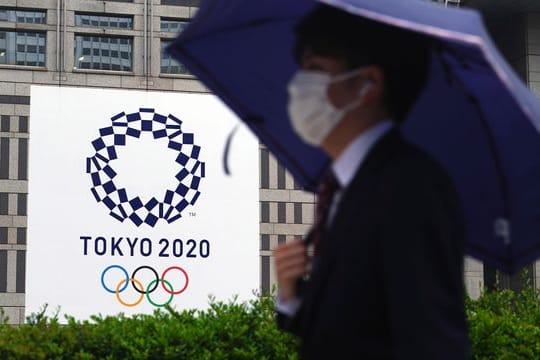 Ein Mann mit Mund-Nasen-Schutz geht im Regen an einem Banner der Olympischen Spiele Tokio 2020 vorbei.