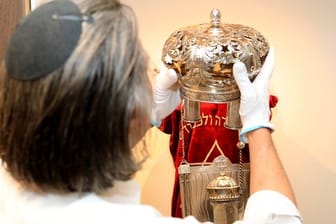 Der Kurator Uri Faber setzt eine Krone auf eine Torarolle mit Mantel im Berend Lehmann Museum in Halberstadt.