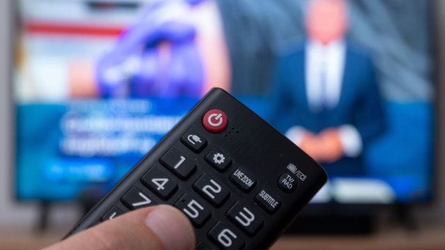 Ein Mann hält eine Fernbedienung vor einen Fernseher, auf dem die Tagesschau läuft. Ein Mann hält eine Fernbedienung vor einen Fernseher, auf dem die Tagesschau läuft.