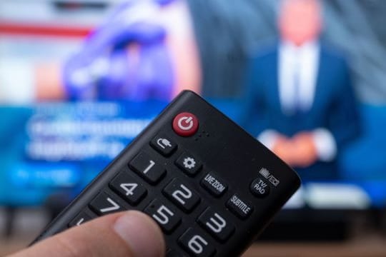 Ein Mann hält eine Fernbedienung vor einen Fernseher, auf dem die Tagesschau läuft.