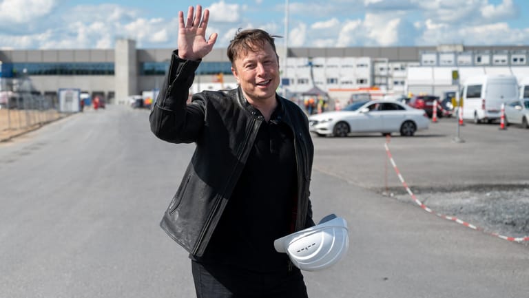 Elon Musk steht auf der Baustelle der Tesla-Fabrik und winkt.