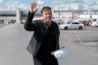 Elon Musk steht auf der Baustelle der Tesla-Fabrik und winkt.