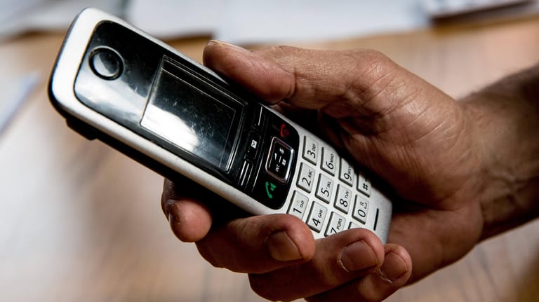 Die Hand eines älteren Menschen hält ein Telefon (Symbolbild): Mit einer Betrugsmasche am Telefon wurde ein Senior in Leverkusen um sein Geld bestohlen.