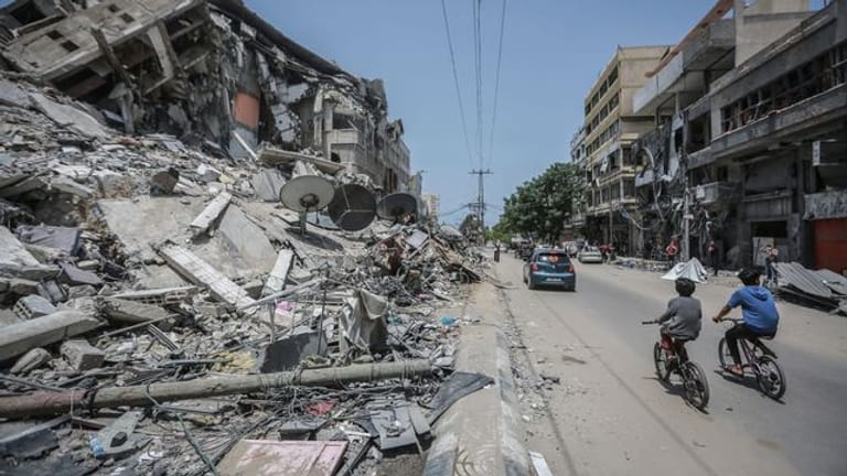 Palästinenser fahren an Gebäuden in Gaza vorbei, die durch israelische Luftangriffe zerstört wurden.