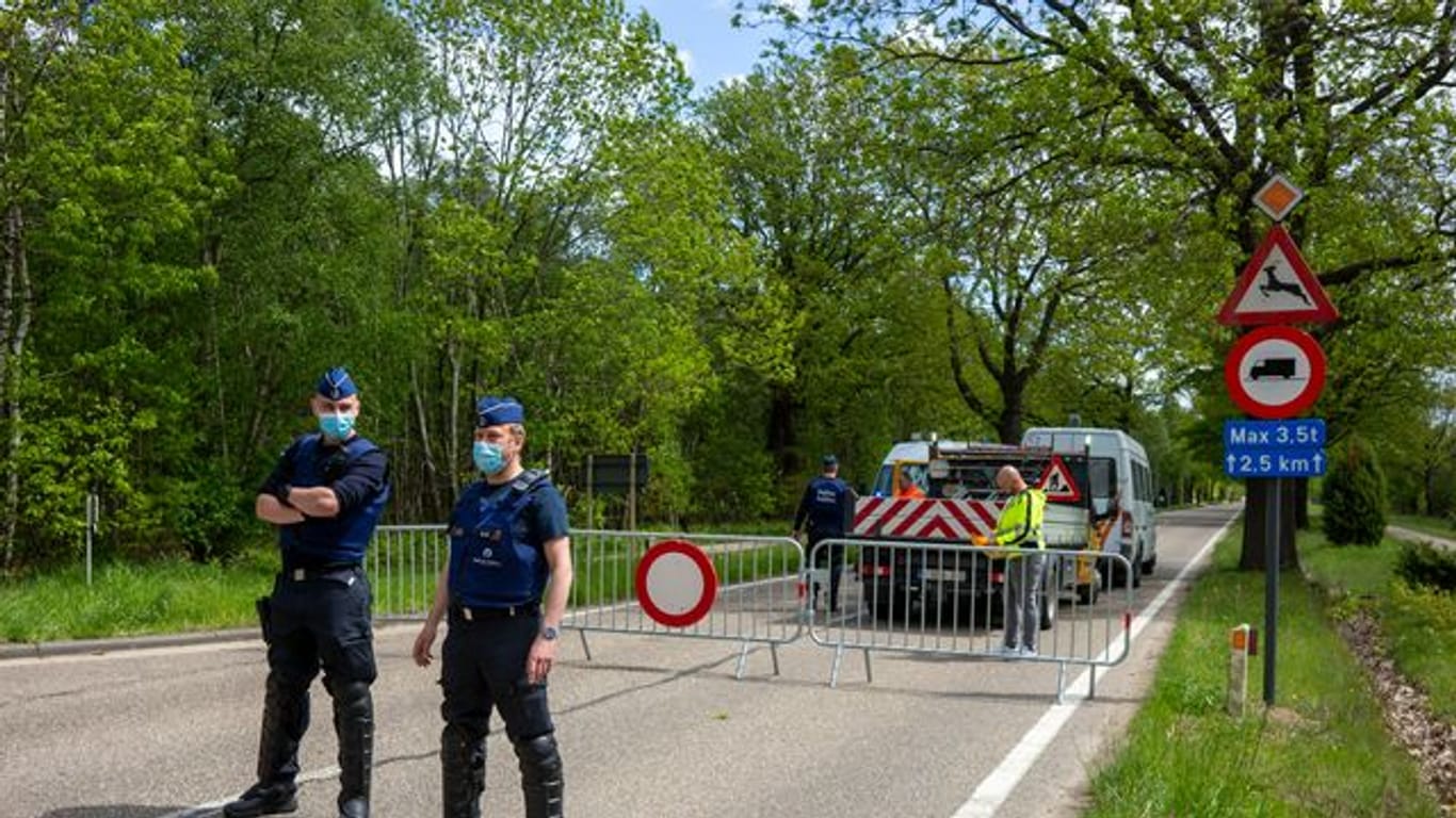 Belgische Polizisten sperren eine Straße in einem Waldstück ab.