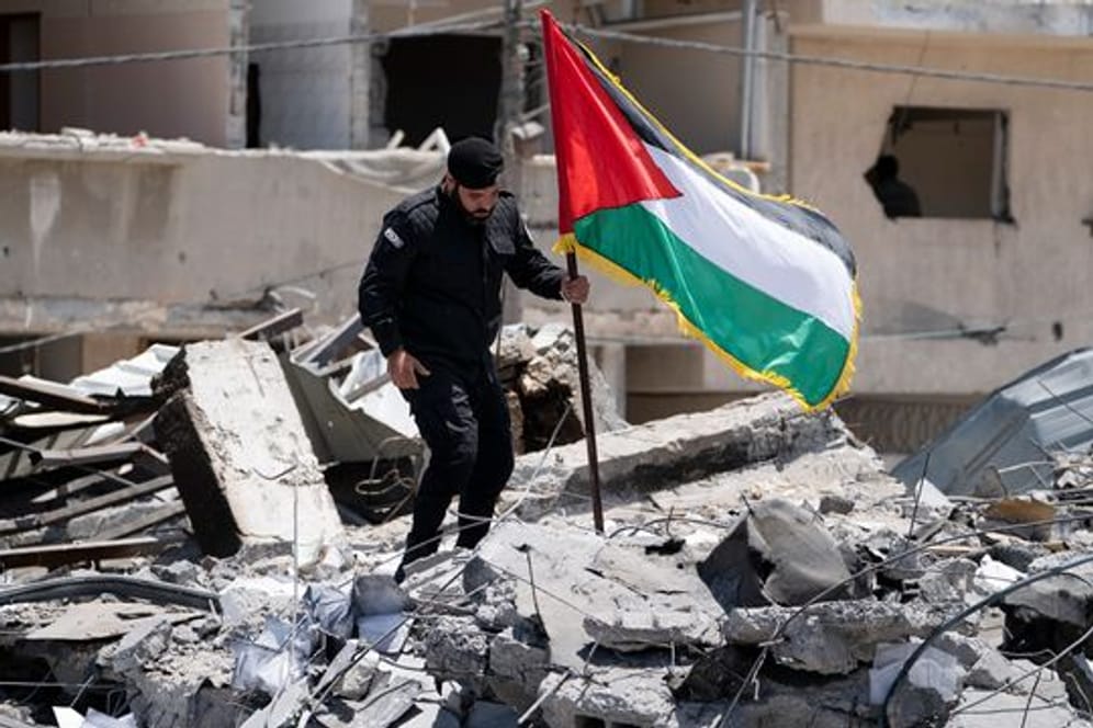Ein Polizist der Hamas entfernt eine palästinensische Fahne von einem Trümmerhaufen eines Bahnhofsgebäudes, das bei Luftangriffen zerstört worden war.