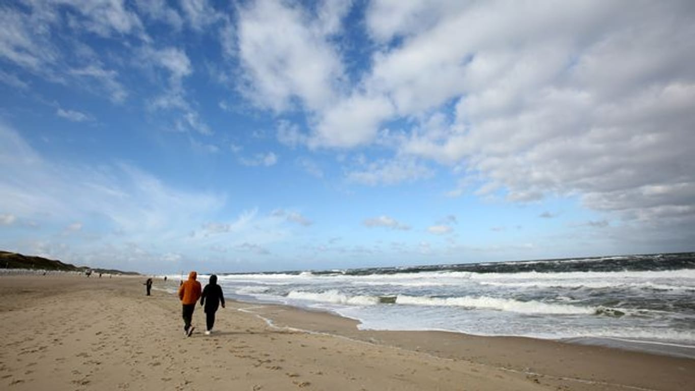 Bei windigem Wetter sind Spaziergänger am Strand von Westerland auf Sylt unterwegs.