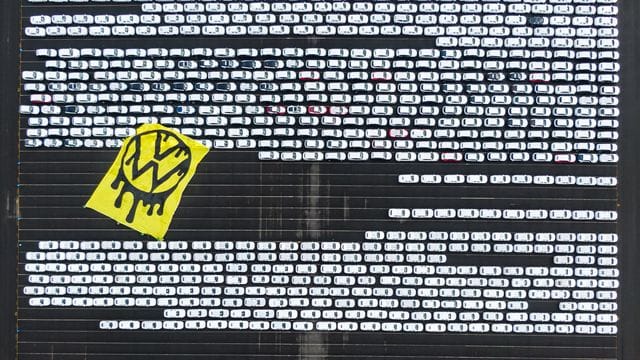 Greenpeace-Aktivisten breiten ein riesiges Protesttransparent über Autos aus, die auf dem Verladeplatz von VW im Emdener Hafen stehen. Greenpeace-Aktivisten breiten ein riesiges Protesttransparent über Autos aus, die auf dem Verladeplatz von VW im Emdener Hafen stehen.