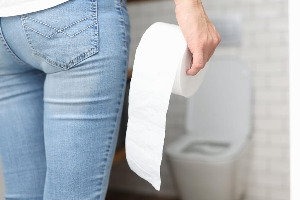 Eine Frau mit Toilettenpapier in der Hand: Vergrößerte Hämorrhoiden können mit verschiedenen Symptomen einhergehen.