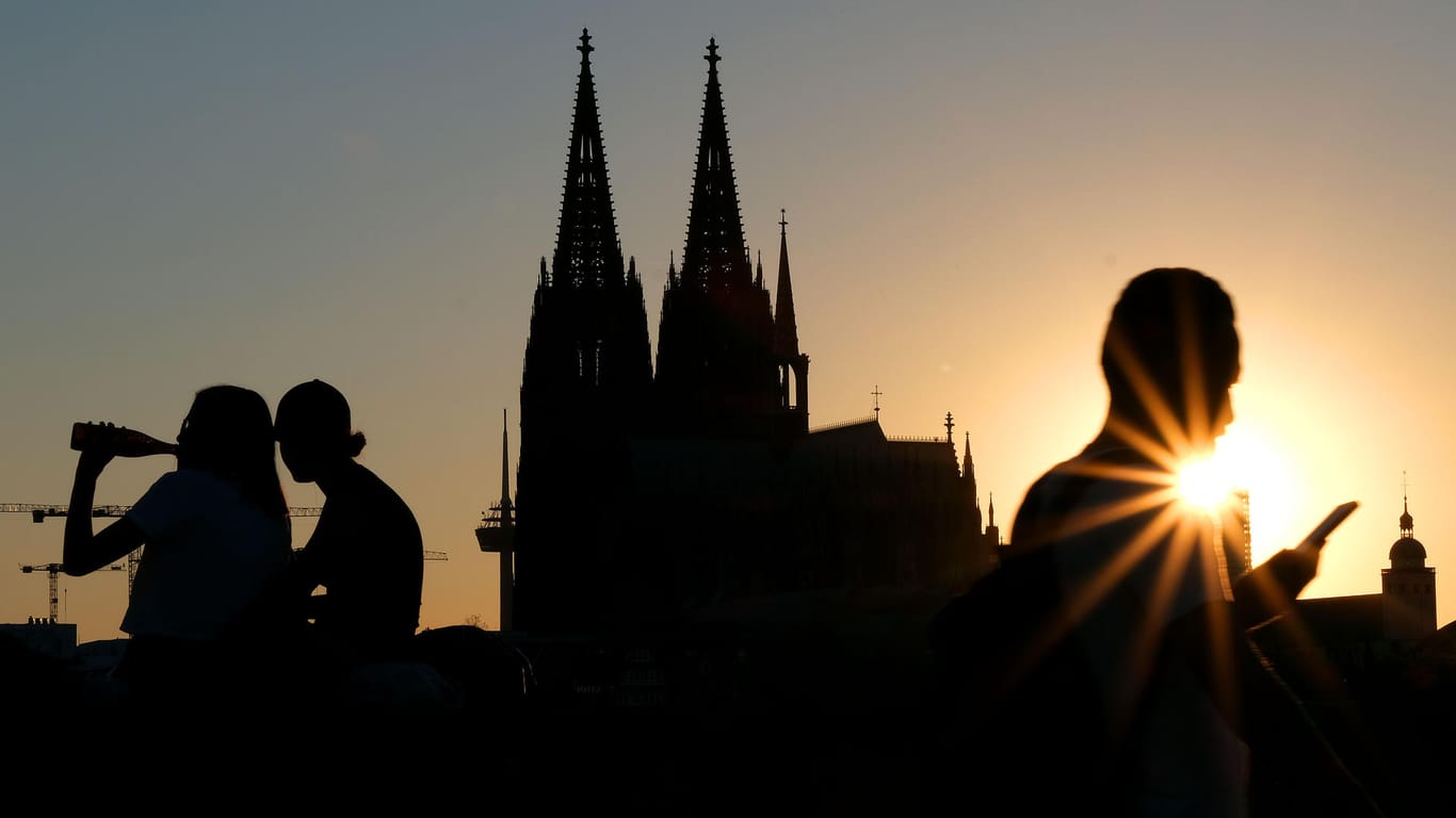 Menschen genießen im Sonnenuntergang am Rheinboulevard vor dem Dom die Abendstimmung: In Köln ist die Inzidenz auf knapp unter 40 gesunken.