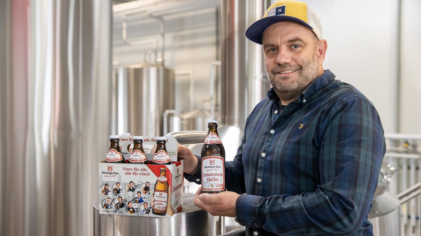 Stefan Stretz, Geschäftsführer der Nürnberger Brauerei Schanzenbräu, hält eine Flasche Bier "Zusammen Halbe" in der Hand neben einem Six-Pack der Sorte: Stretz hat die "Zusammen Halbe" mit acht weiteren Nürnberger Brauereien zusammen entwickelt und gebraut.
