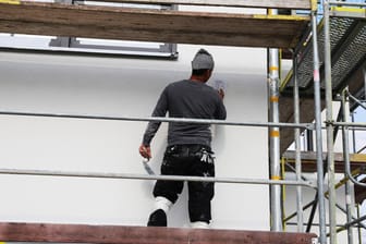 Maler arbeitet an der Fassade eines neuen Wohnhauses (Symbolbild): Die Materialien im Handwerk werden immer knapper und die Preise für Kunden somit immer teurer.