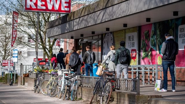 Menschen warten in einer Schlange vor einem Rewe Markt