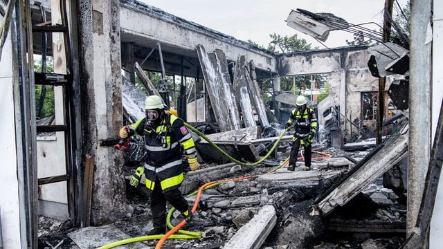 Feuerwehrmänner laufen durch die zerstörte Autowerkstatt: Anwohner wurden wegen der starken Rauchentwicklung gebeten, Fenster und Türen geschlossen zu halten.