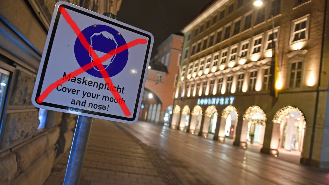 Das Schild mit den Hinweis zur Maskenpflicht in der Fußgängerzone von München ist durchgestrichen (Archivbild/Bildmontage): In der Stadt gilt nur noch an einzelnen Plätzen die Maskenpflicht.