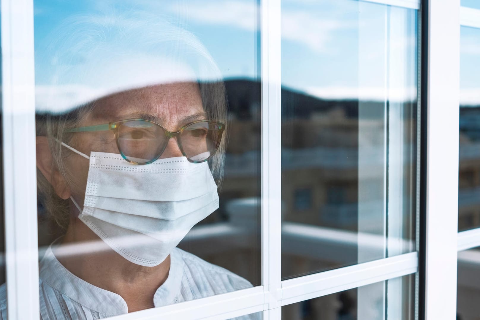 Seniorin blickt aus dem Fenster: Noch immer warten einige Menschen trotz ihrer Priorisierung auf einen Impftermin.