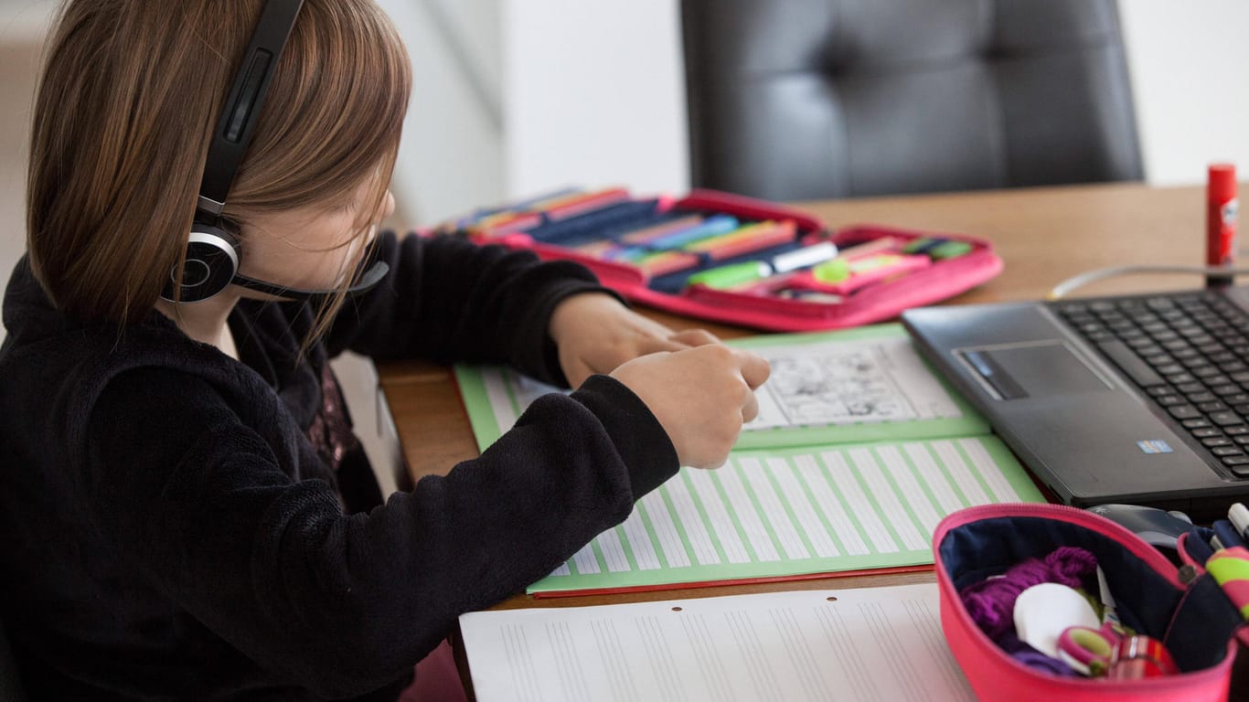 Ein Kind sitzt an einem Wohnzimmertisch im Elternhaus und löst Aufgaben in einem Schulheft (Symbolbild): Die Bildschirmzeit hat sich bei den Kindern erhöht.
