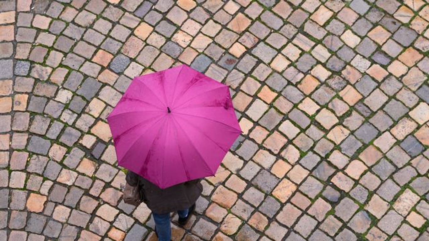 Eine Passantin geht mit ihrem Regenschirm über einen Platz.