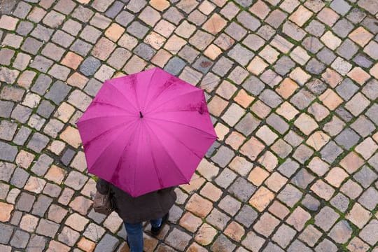 Eine Passantin geht mit ihrem Regenschirm über einen Platz.