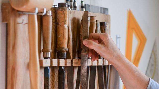 Ein Handwerker greift in einer Werkstatt nach einem Werkzeug Ein Handwerker greift in einer Werkstatt nach einem Werkzeug