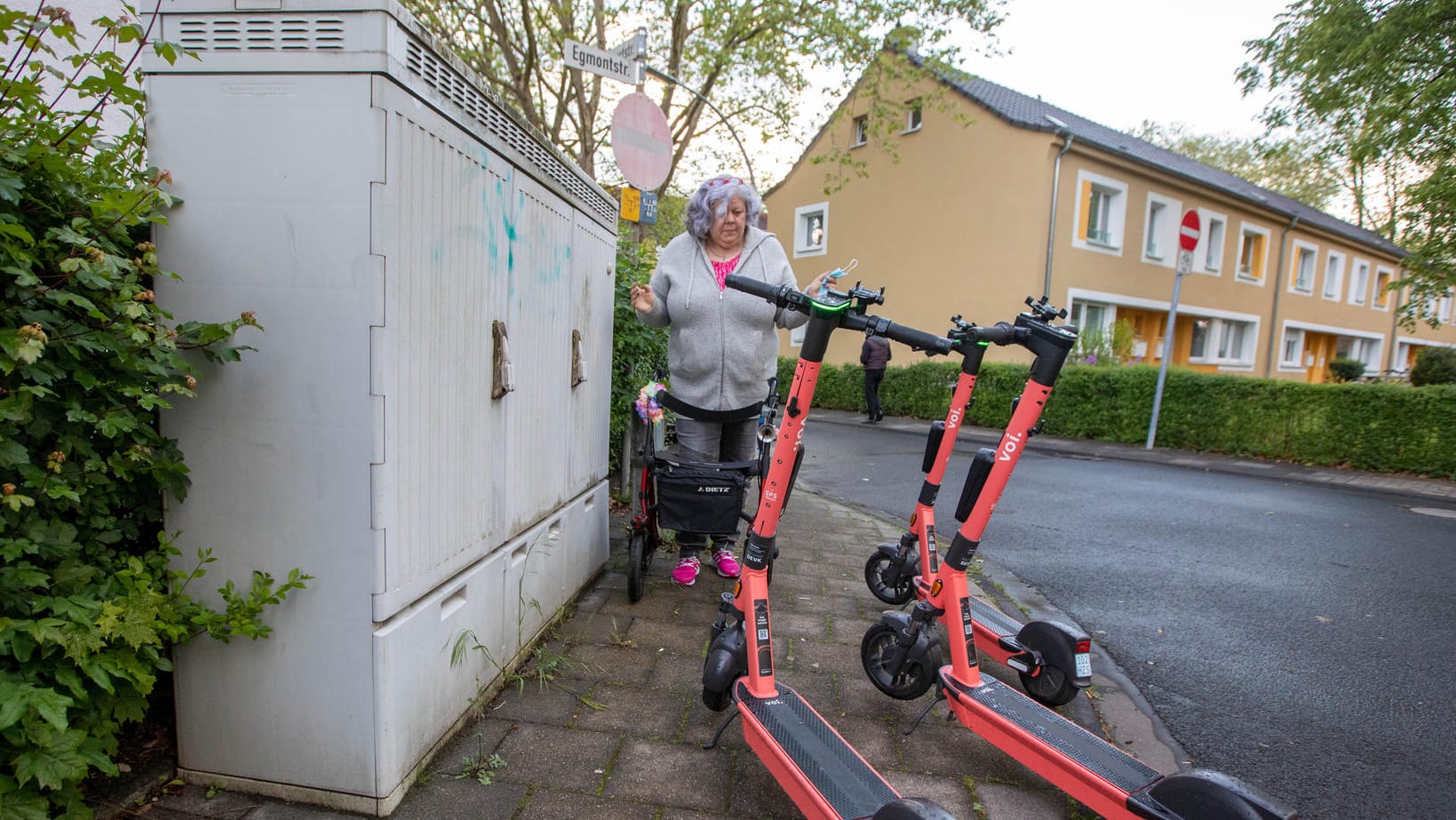 Weg versperrt: Gabriele Matzantke versucht in Porz mit ihrem Rollator auf dem Gehweg an den dort abgestellten E-Scootern vorbeizukommen.