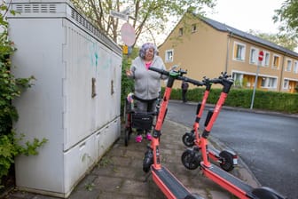Weg versperrt: Gabriele Matzantke versucht in Porz mit ihrem Rollator auf dem Gehweg an den dort abgestellten E-Scootern vorbeizukommen.