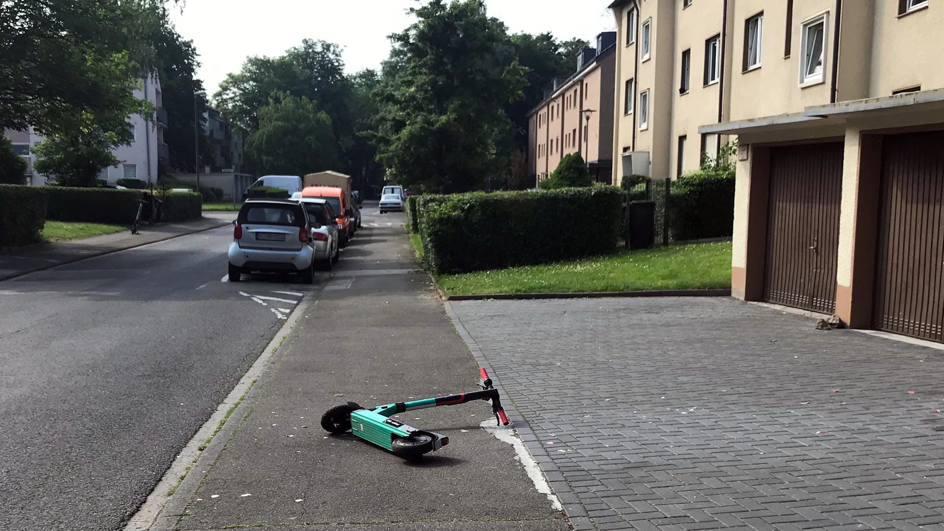 Ein E-Scooter liegt mitten auf dem Gehweg vor Garagen im Kölner Stadtteil Porz-Eil.