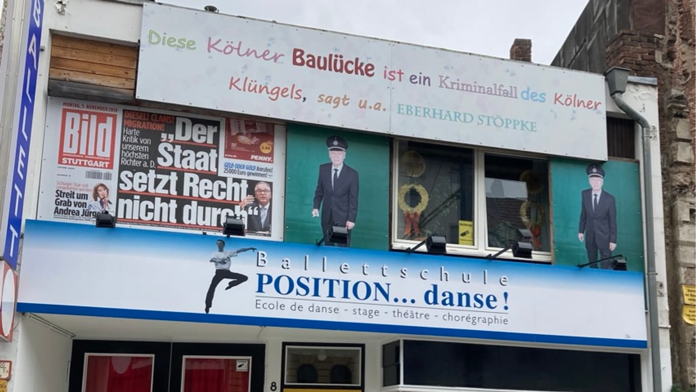 Die Ballettschule auf einem angrenzenden Grundstück: Hier hängen alte Fotos, die den Eigentümer Eberhard Stöppke als Polizisten zeigen, sowie der Satz "Diese Kölner Baulücke ist ein Kriminalfall des Kölner Klüngels"