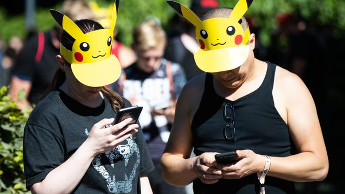 Zwei Teilnehmer mit Pokemon-Sonnenschutz spielen im Westfalenpark in Dortmund auf ihren Handys "Pokemon Go" (Archivbild vom 30.
