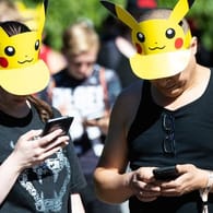 Zwei Teilnehmer mit Pokemon-Sonnenschutz spielen im Westfalenpark in Dortmund auf ihren Handys "Pokemon Go" (Archivbild vom 30.