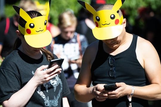 Zwei Teilnehmer mit Pokemon-Sonnenschutz spielen im Westfalenpark in Dortmund auf ihren Handys "Pokemon Go" (Archivbild vom 30.