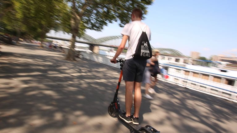 Ein Mann fährt mit einem E-Roller am Ufer des Rheins in der Kölner Innenstadt (Archivbild): Offenbar sind ins Wasser geworfene E-Scooter in der Domstadt ein massives Problem.