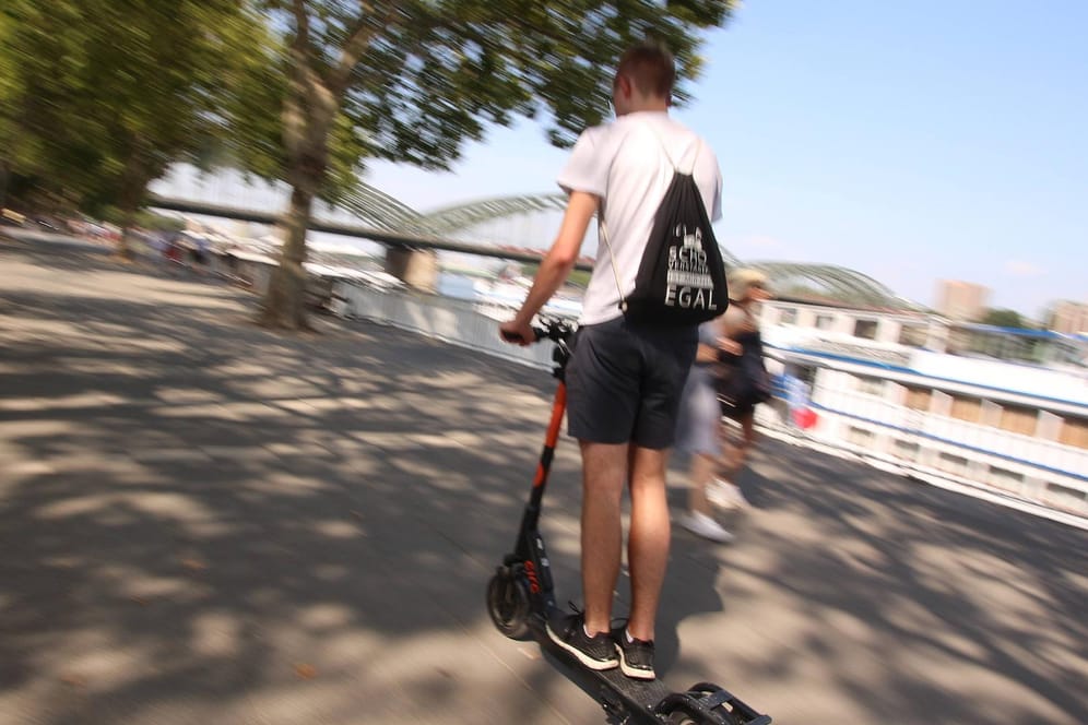 Ein Mann fährt mit einem E-Roller am Ufer des Rheins in der Kölner Innenstadt (Archivbild): Offenbar sind ins Wasser geworfene E-Scooter in der Domstadt ein massives Problem.
