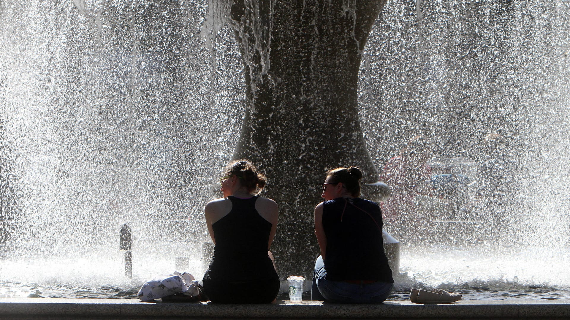 Sommerlich warmer Tag in Frankfurt: Frauen in sommerlicher Kleidung sitzen am Brunnen vor der Alten Oper am Opernplatz und genießen ein Fußbad.