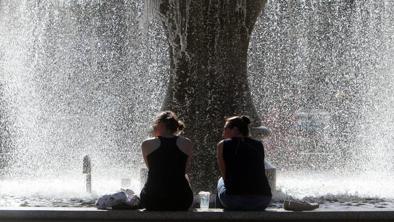 Sommerlich warmer Tag in Frankfurt: Frauen in sommerlicher Kleidung sitzen am Brunnen vor der Alten Oper am Opernplatz und genießen ein Fußbad.