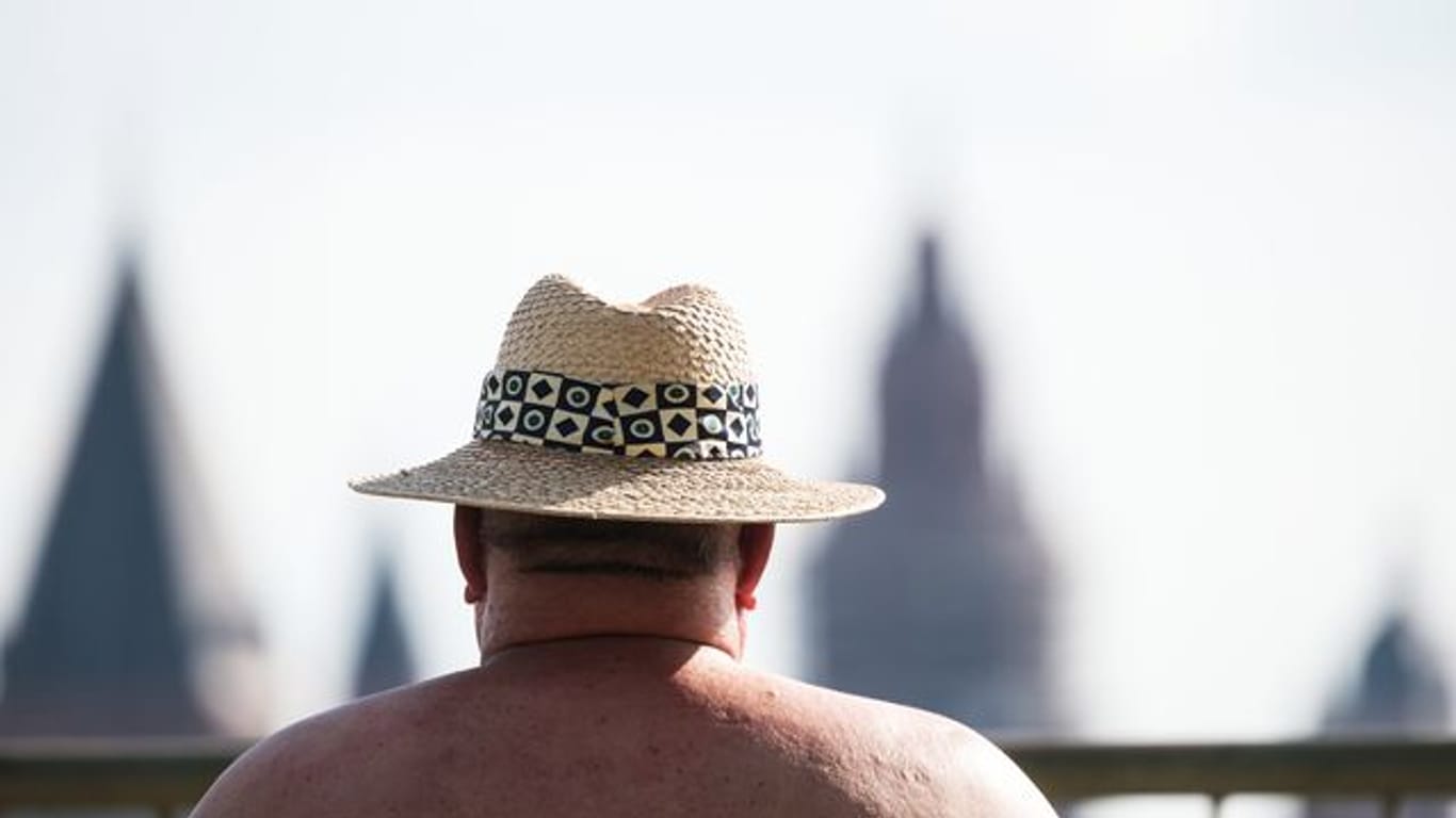 Ein Mann sitzt mit Hut am Rheinufer (Symbolbild): Empfindliche Menschen sollten keine anstrengenden Tätigkeiten verüben.